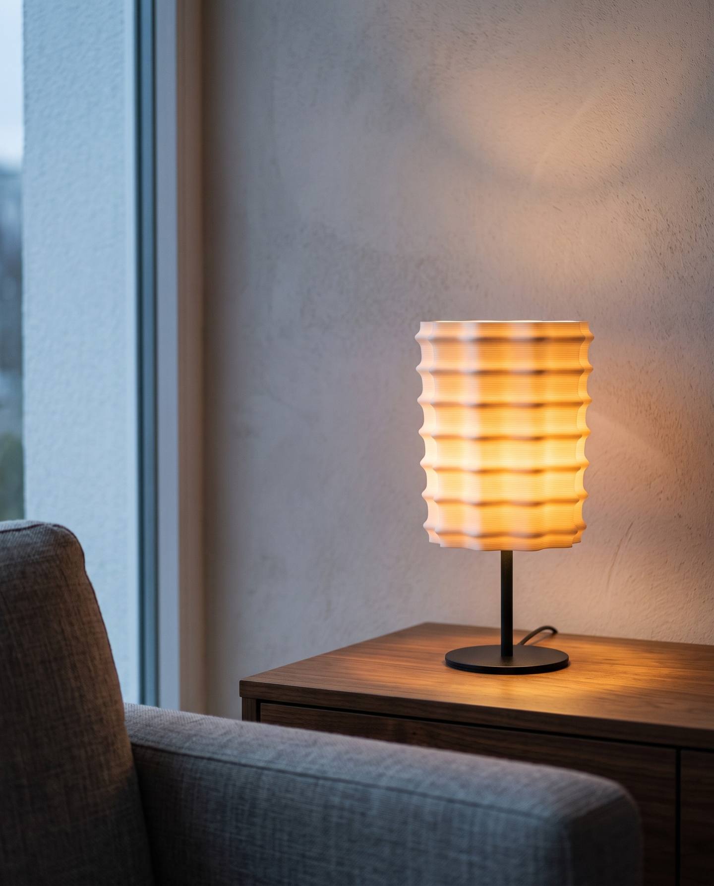 A 3D printed lampshade glowing warm on a walnut side table at dusk, the fine layer lines visible through the light