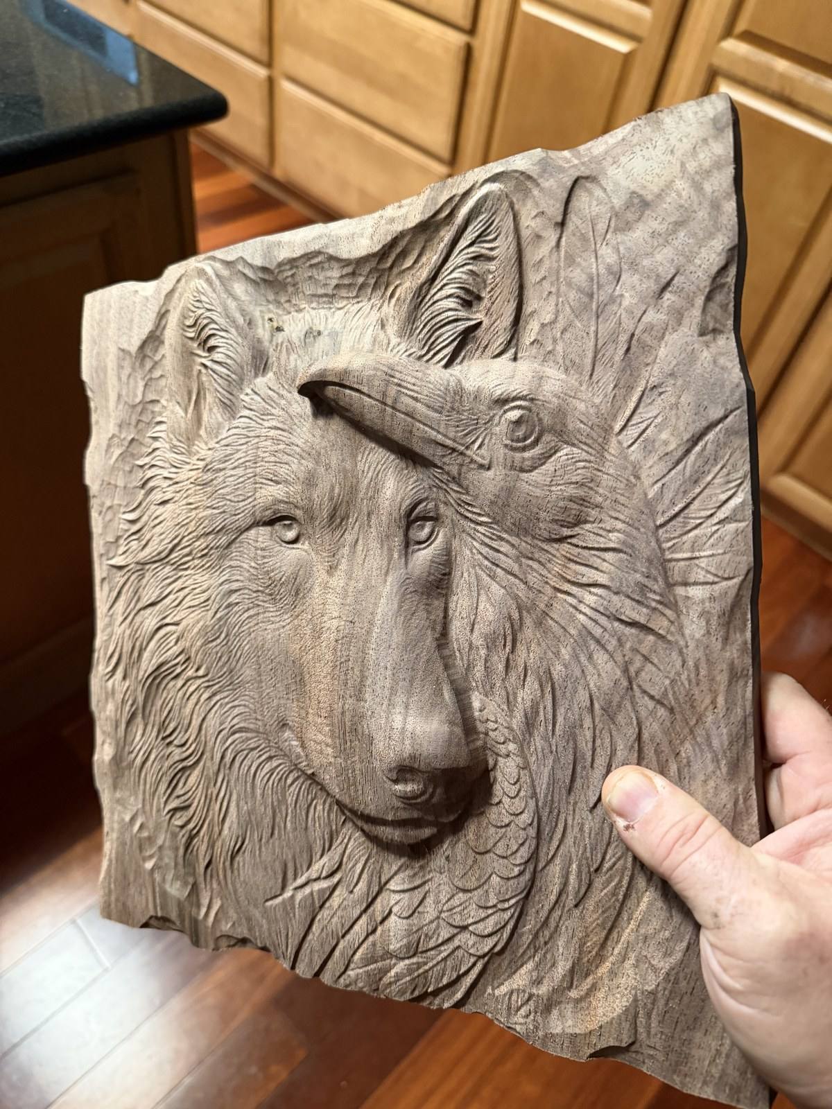 The bare walnut wolf and raven relief just off the machine after the 1/16 inch tapered ball nose finishing pass, held up in a kitchen
