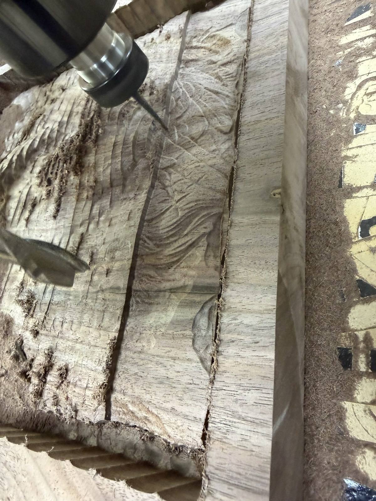 A tapered ball nose bit cutting the finishing pass across the roughed walnut, the finished detail appearing behind it
