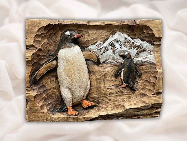 Bas-relief wood carving of two gentoo penguins standing before snowy mountains on a carved panel