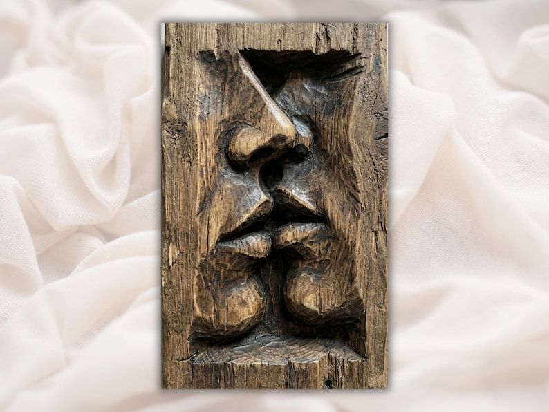 Bas-relief wood carving of two abstract faces in profile meeting in a kiss, dark grain texture