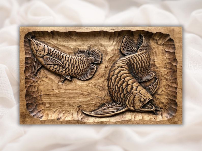 Carved wood bas-relief of two arowana fish with detailed scales on a chiseled textured panel