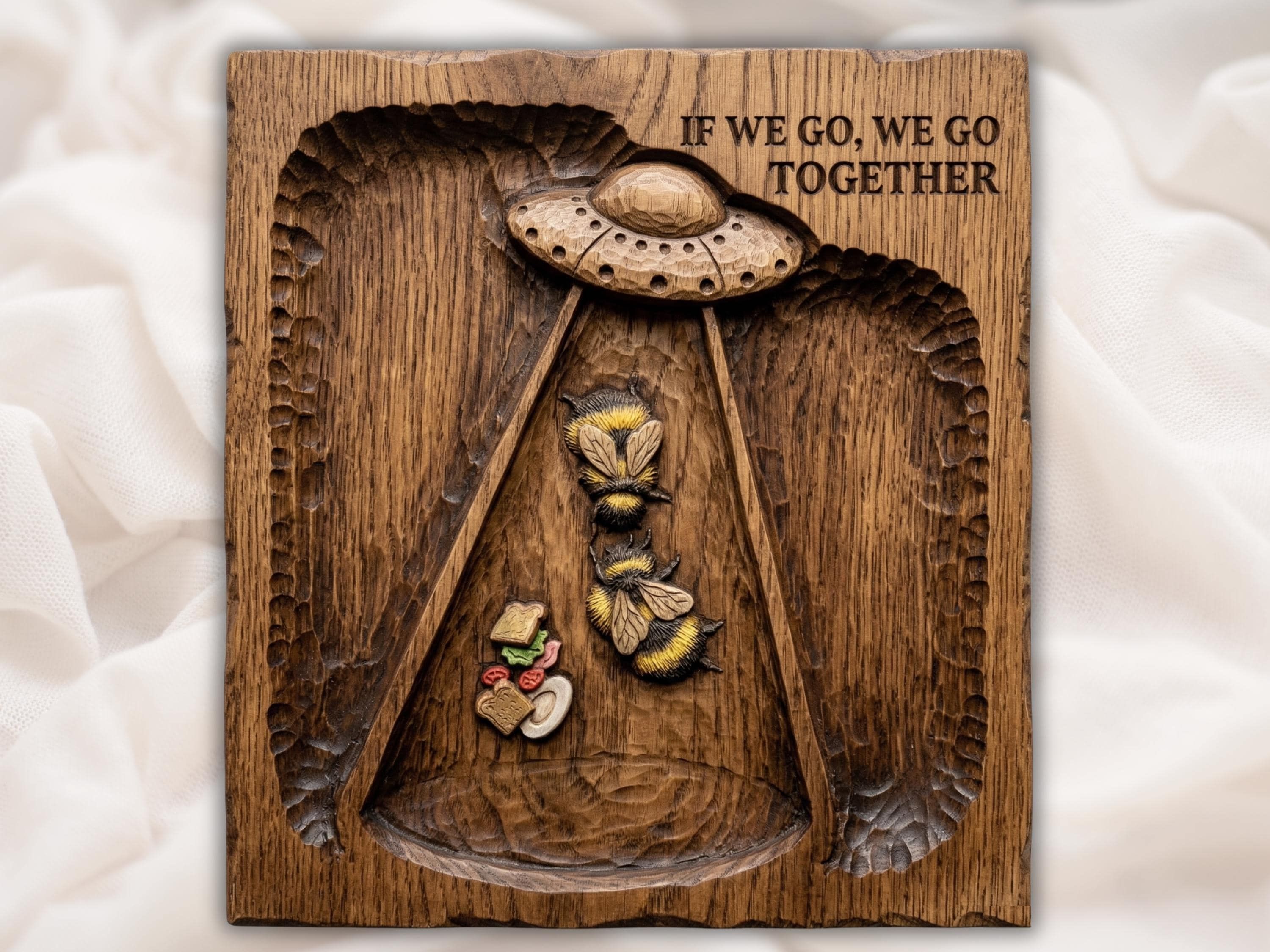 Wood bas-relief of a UFO beaming up two bumblebees over a falling sandwich with carved text