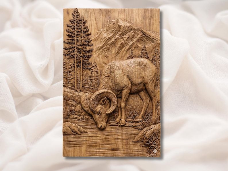 Carved wood bas-relief of a bighorn ram drinking from a river with pine trees and a mountain peak