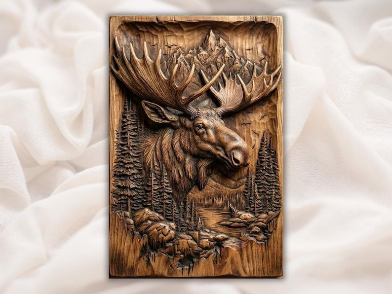 Carved wood bas-relief of a bull moose head with antlers, pine trees, river, and mountain peak behind.