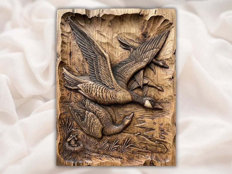 Wood bas-relief carving of two Canada geese flying low over a lake with a nesting goose in the reeds
