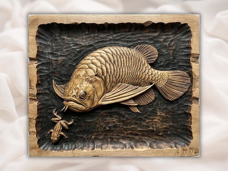 Carved wood bas-relief of an arowana fish with detailed scales and a small newt on a deep textured background