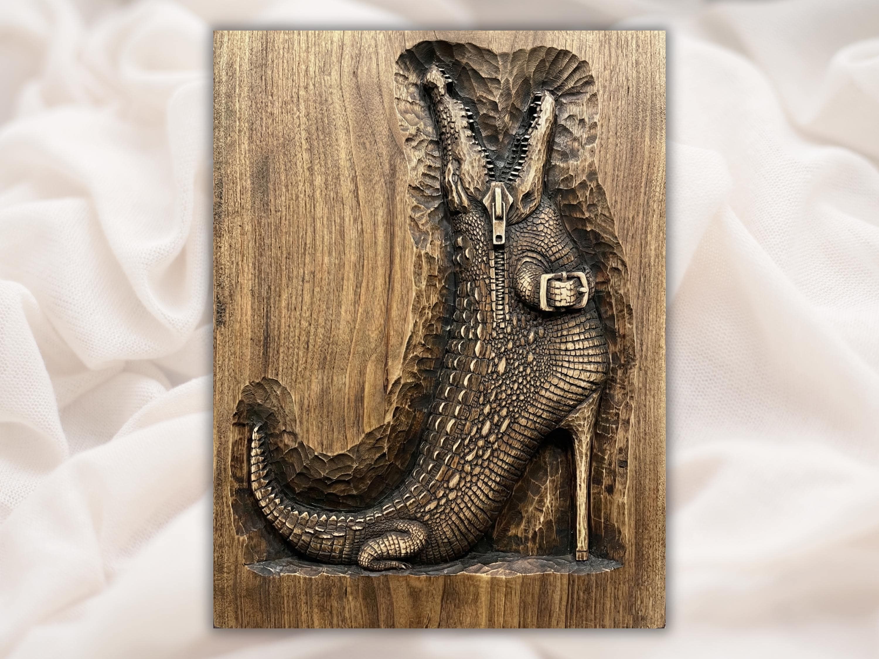 Bas-relief wood carving of a crocodile emerging through an open zipper, scaled body and clawed foot