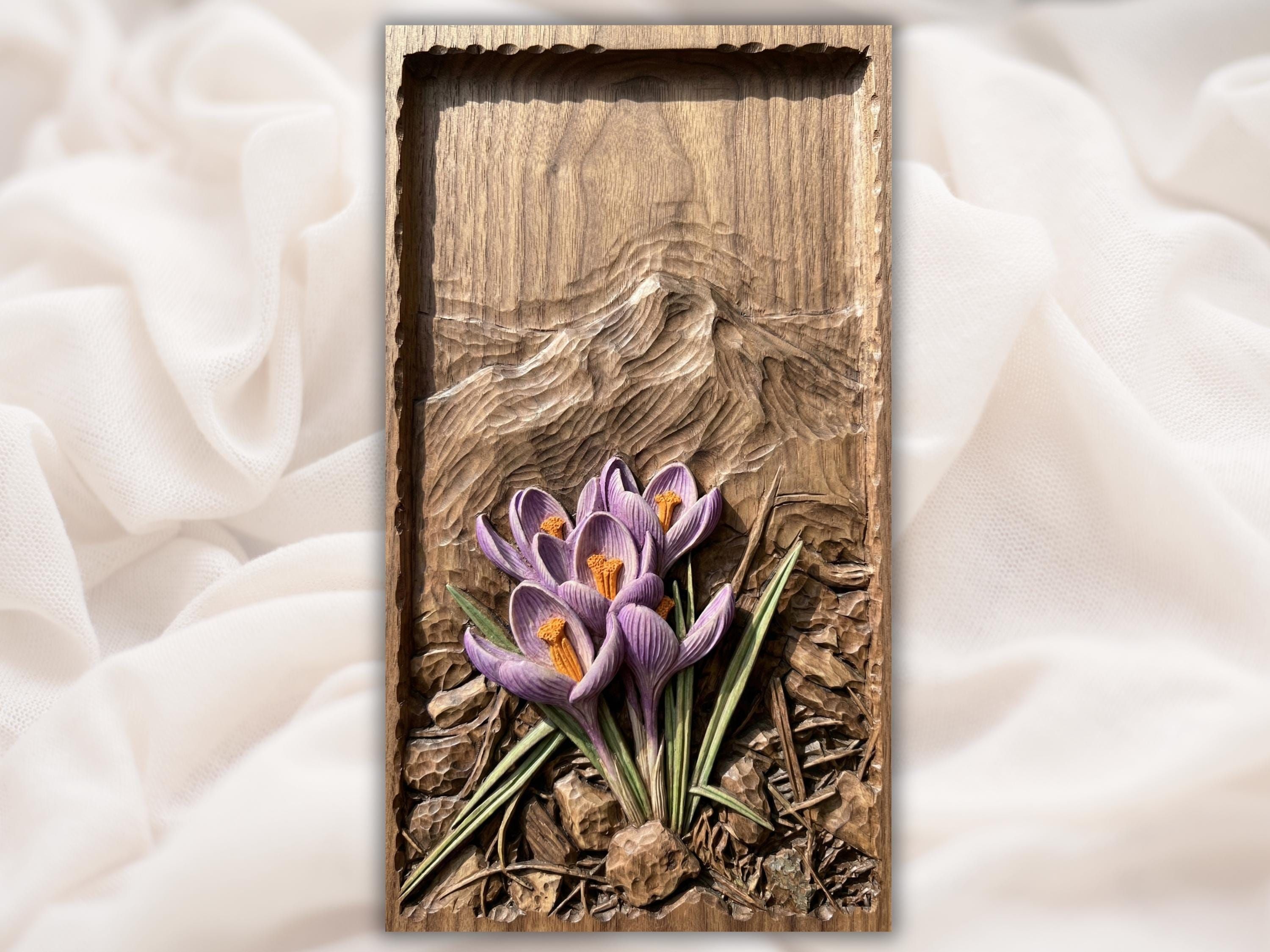 Carved wood bas-relief of purple crocus flowers with orange stamens rising from textured soil and stones