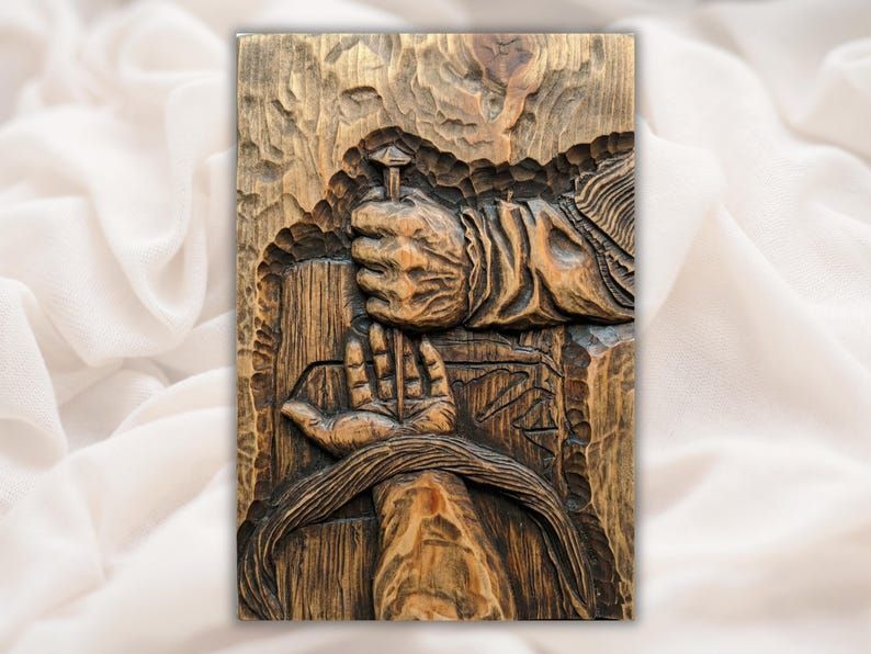 Carved wood relief of a nailed hand gripping a cross beside an open palm, crucifixion scene