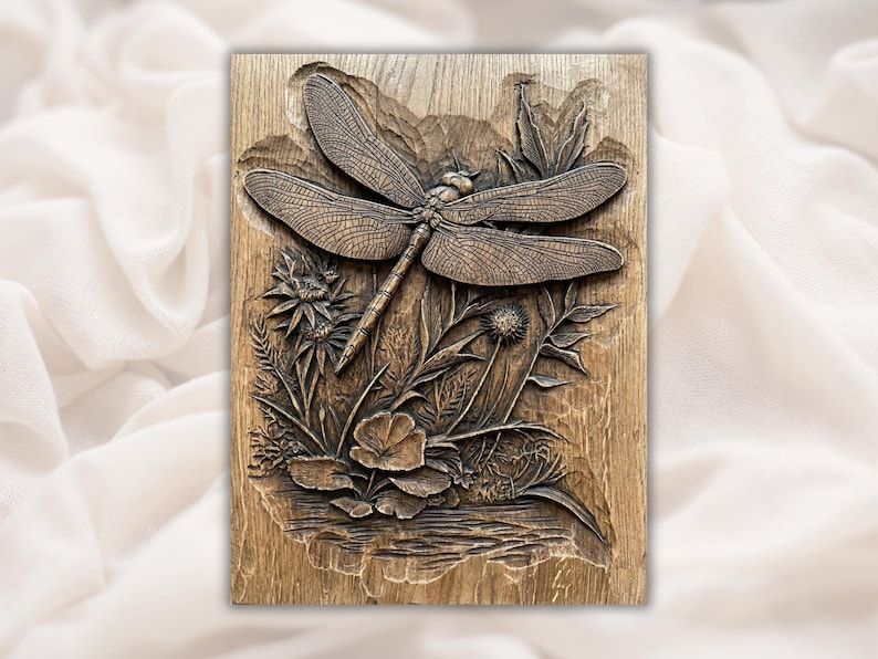 Carved wood bas-relief of a dragonfly with spread wings resting above wildflowers, thistles, and grasses