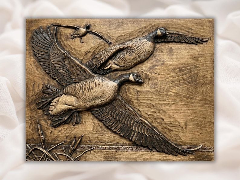 Carved wood bas-relief of three Canada geese flying over cattails and marsh grass with feather detail