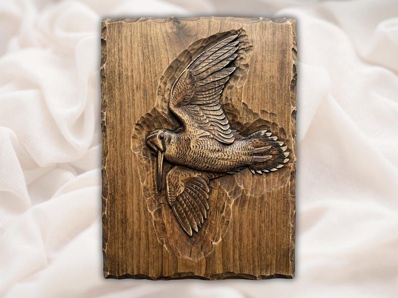 Carved wood bas-relief of a woodcock in flight with spread wings, feather detail, and a long bill