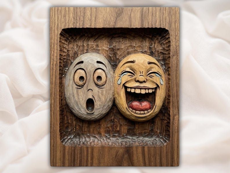 Wood bas-relief of two faces, one laughing and crying, one shocked, inside a recessed carved frame.