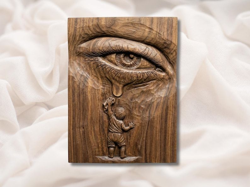 Carved wood relief of a large eye shedding a tear with a small child below reaching up to catch it