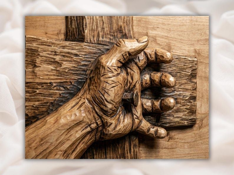 Bas-relief wood carving of a hand nailed to a rough wooden cross, fingers curled near the nail