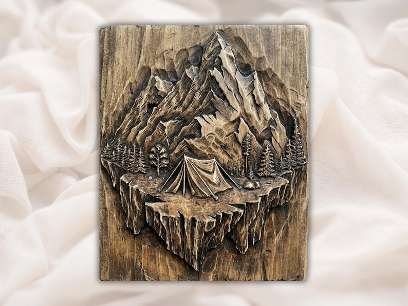 Carved wood relief of a mountain peak, pine trees and a camping tent on a floating cliff
