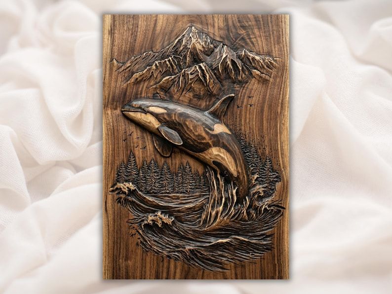 Carved wood relief of an orca whale breaching over ocean waves with pine trees and mountains behind