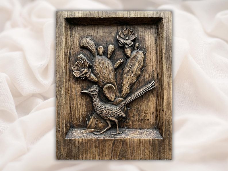 Carved wood bas-relief of a roadrunner with prickly pear cactus pads and desert flowers in a shadowbox frame