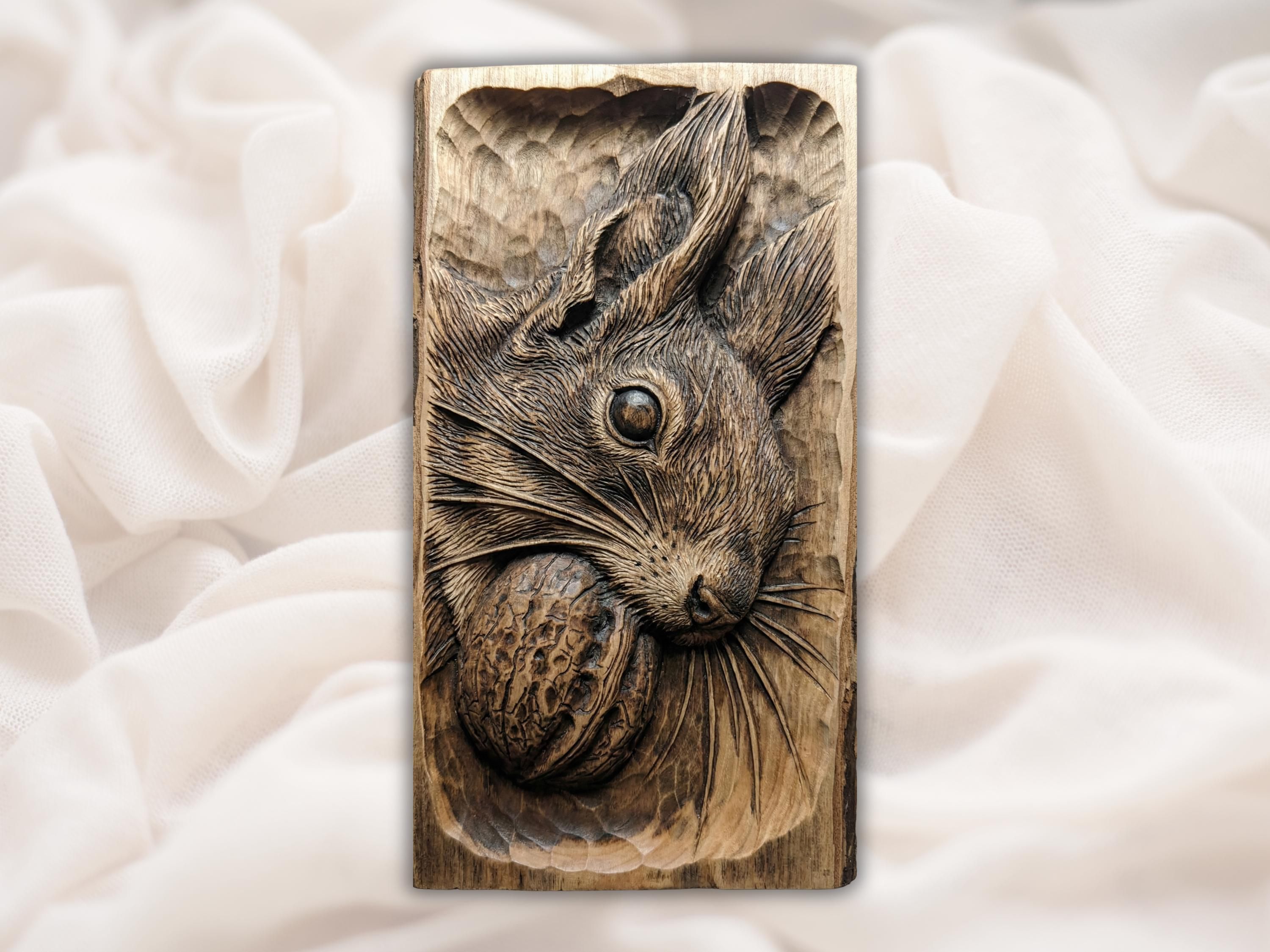 Carved wood bas-relief of a squirrel holding a walnut, detailed fur and a round dark eye