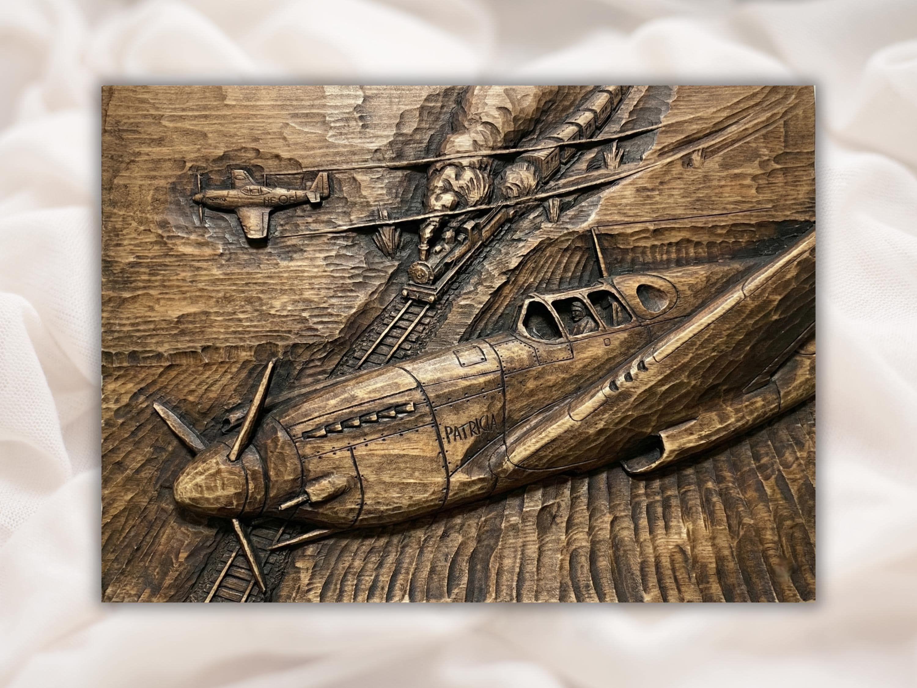 Bas-relief wood carving of a WWII fighter plane named Patricia with a steam train climbing a mountain behind it