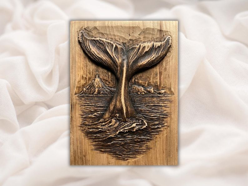Bas-relief wood carving of a whale tail rising from ocean waves with rocky islands in the background