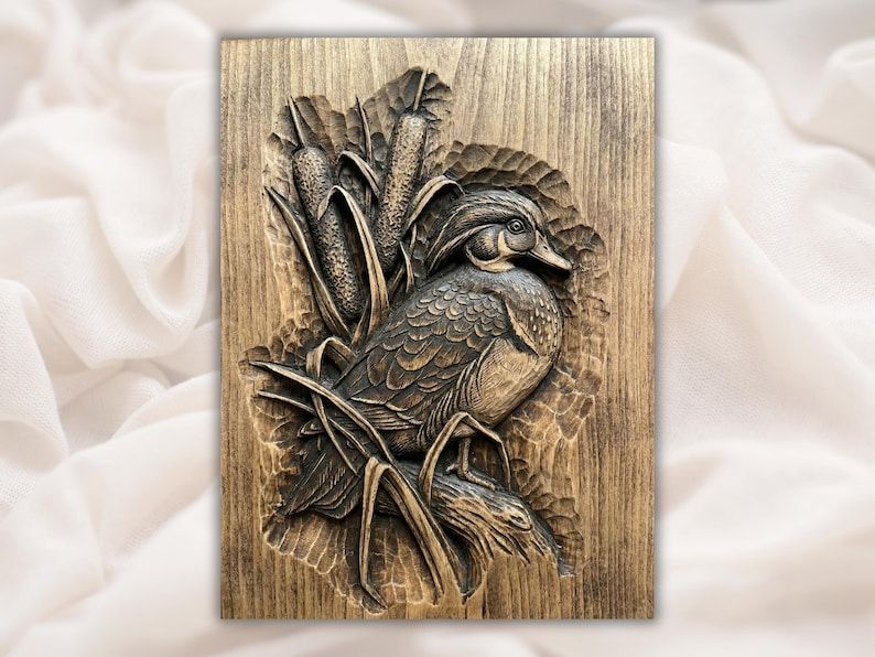 Carved wood relief of a wood duck sitting among cattails and reeds with a chiseled grain background